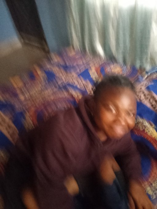 A blurry photo of a young person in a maroon hoodie smiling while sitting on a patterned blue and orange couch.
