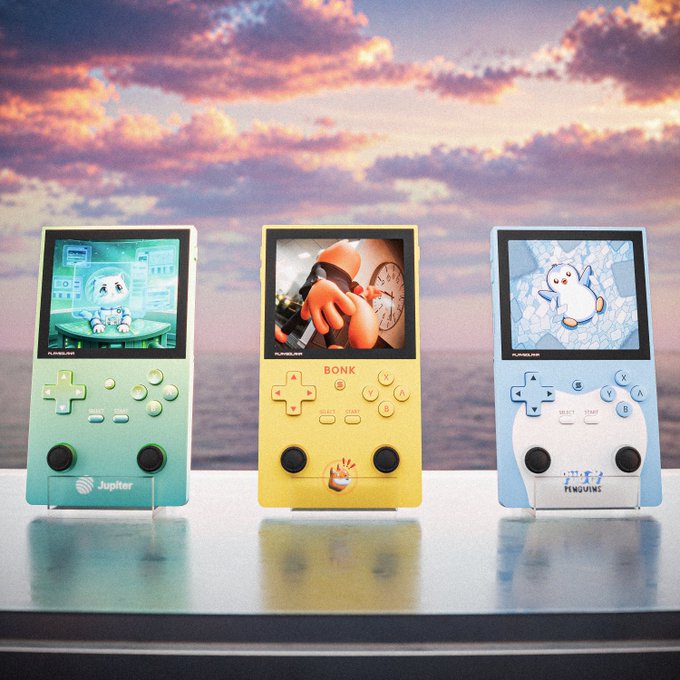 Three Playdate handheld consoles stand side by side against a pastel sky, labeled “Jupiter,” “BONK,” and “PENNYWISE.” The lineup of three devices matches the post’s caption, “Trifecta.”