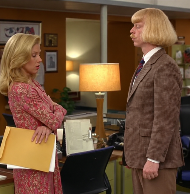 A blonde woman holding a manila folder looks down disapprovingly at a man with a blonde bowl-cut wig and mustache wearing a brown suit in an office setting.