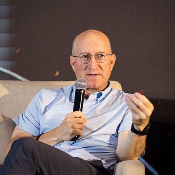 An image of Eli Ben-Sasson, the CEO of StarkWare, speaking into a microphone while seated and gesturing with his hand during what appears to be a panel discussion or interview.