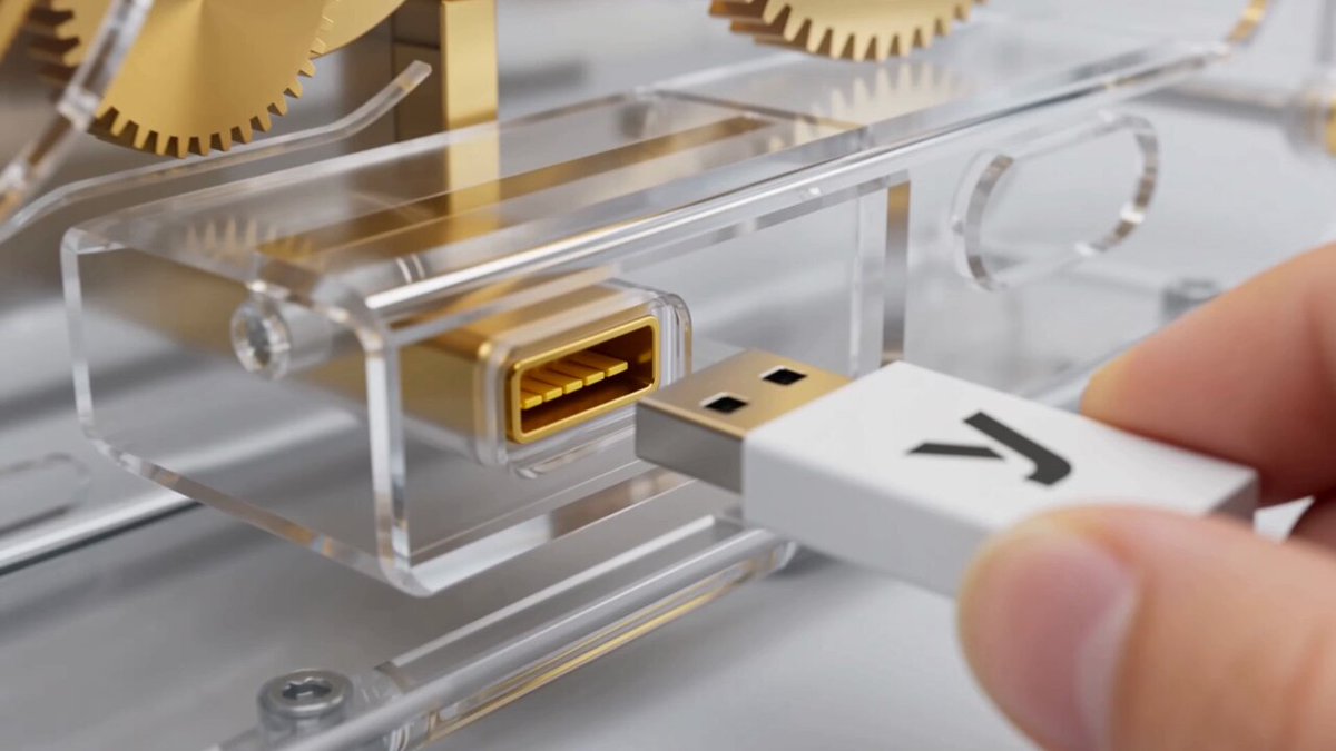The image shows a person's hand holding a white USB cable with a gold connector, which appears to be plugged into an electronic device or machine. The focus of the image is on the USB cable and its connection to the device.