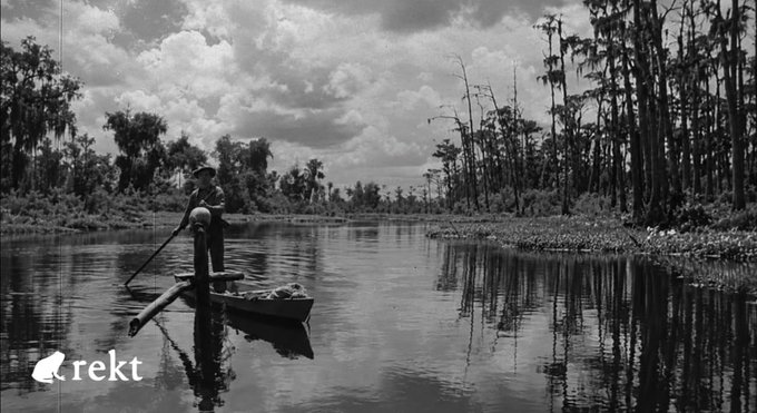 A black-and-white photograph shows a lone figure standing in a small boat, poling through a calm swamp lined with Spanish moss-draped trees, evoking a quiet, isolated journey. The image's watermark reads "rekt," tying the visual to a post about a $320 million exploit on the Liquid Network, where an attacker minted ~4,000 unbacked L-BTC through a cryptographic flaw and controversially returned most of the funds, leaving the crypto community debating whether it was theft or an ethical bounty.