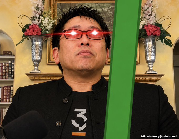 An Asian man wearing glasses with digitally added glowing red laser eyes, standing in an elegant room with floral arrangements and a framed painting, with a green graphic overlay on the right side and the text 'bitcoindawg@primal.net' in the corner.