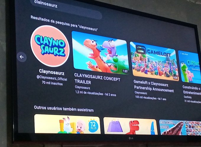 A TV screen displaying YouTube search results for 'claynosaurz', showing the channel with 70 mil inscritos and video results including 'CLAYNOSAURZ CONCEPT TRAILER' and 'Gameloft x Claynosaurz Partnership Announcement'.