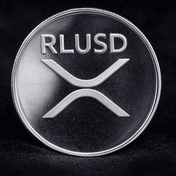 A close-up image of a silver XRP/Ripple cryptocurrency coin against a black background.