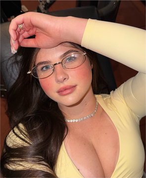 The image shows a young woman wearing glasses and a light yellow top, with a diamond necklace. This image relates to the accompanying post as it's implied she is a representation of success or reaching peak potential, similar to how Bitcoin, Apple, Amazon, and Messi are presented in their respective successful years.