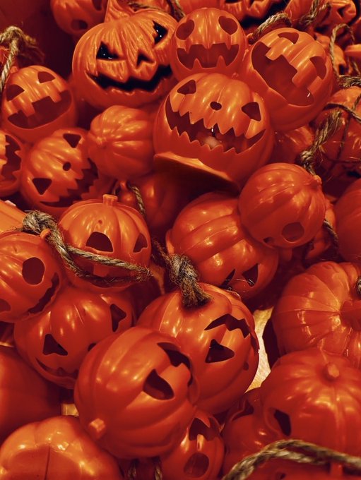 A close-up image shows a pile of orange plastic jack-o'-lantern Halloween buckets with carved smiling faces, stacked together.