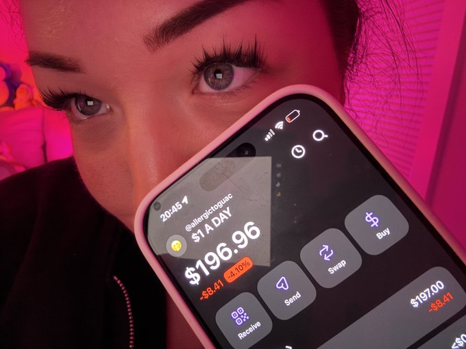 Close-up of a person under pink lighting holding a smartphone displaying a crypto app showing $ADAY (Allegoricdog) at $196.96, down $8.41 (-4.10%), with Buy, Swap, Send, and Receive buttons.