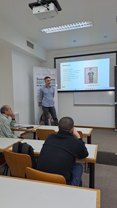A man gives a presentation in a classroom with a projector screen displaying an Ethereum-themed slide titled 'Ethereum' and a banner reading 'Sumate como alumno en tu universidad'.