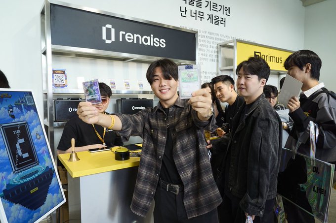 Several young men at a booth labeled 'rendaiss' holding up what appear to be collectible cards, with an 'Optimus' sign visible in the background.