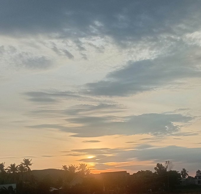 A serene sunrise over a tropical landscape with silhouetted palm trees and distant mountains, paired with a Vietnamese morning market update noting Bitcoin dropping below $64.3K and advising calm observation amid market sensitivity. The peaceful dawn imagery contrasts with the message's caution against fear and FOMO in volatile crypto trading.