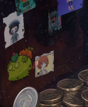 A dark surface displaying various small illustrated stickers or trading cards, including a green creature and a character with orange hair, alongside metallic coins.