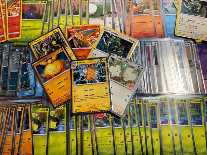 The image shows a collection of Pokemon cards spread out on a table, with some cards overlapping each other. The cards are predominantly yellow and orange, featuring various Pokemon characters such as Pikachu, Eevee, and Bulbasaur. The text "Cosmos Holo Galore" is visible in the image, which could be related to the post about the collection of Pokemon cards or possibly a description of the cards themselves.

The cards appear to be organized by type or series, with some cards grouped together while others are spread out on the table. This arrangement allows for easy browsing and selection of specific cards based on their design or theme. The image captures the essence of the post about Pokemon cards, showcasing a diverse collection that appeals to fans of the popular video game franchise.