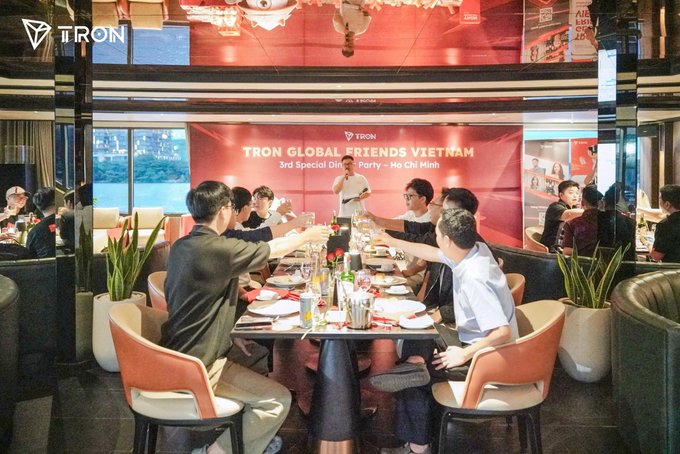 A group of people gathered around a dining table at a restaurant event, with a red backdrop reading 'TRON GLOBAL FRIENDS VIETNAM 3rd Special Dinner Party - Ho Chi Minh' and the TRON logo visible.