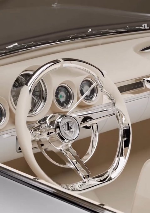 The image features a car with a steering wheel that has a silver finish, giving it an elegant appearance. The interior of the car appears to be white as well, which complements the silver color of the steering wheel. The background of the image is blurred, drawing attention to the car and its details.