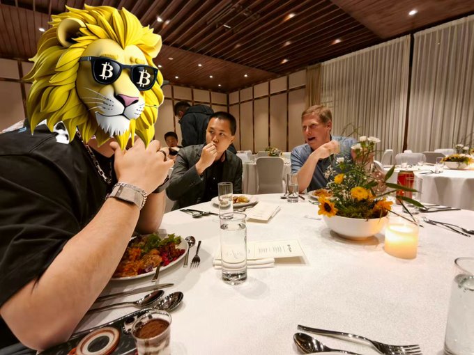 A crypto enthusiast wearing a Bitcoin sunglasses lion mascot head sits at a fine dining table with two other men, humorously promoting the post's message that investors who can't afford 21 BTC should settle for 21 ZEC instead.