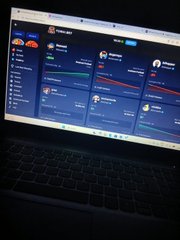 A laptop screen displays the TeamSpeak client interface in a dark room, showing channel listings and user avatars.