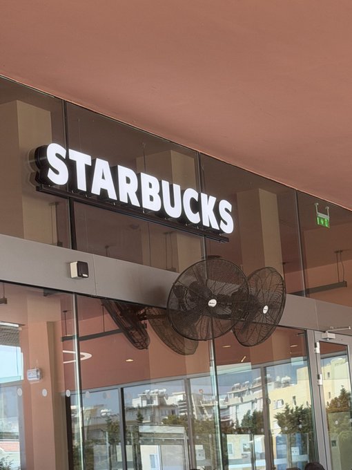 The illuminated 'STARBUCKS' storefront sign with large industrial fans visible through the glass windows below.