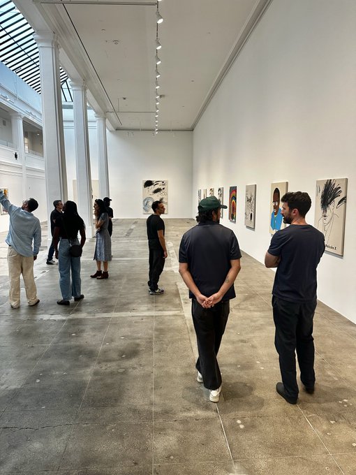 Visitors viewing artwork in a modern art gallery with white walls, polished concrete floors, and tall columns.