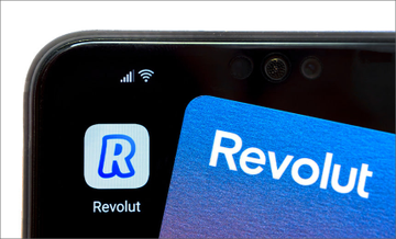 Close-up of a smartphone displaying the Revolut app icon alongside a blue Revolut bank card.