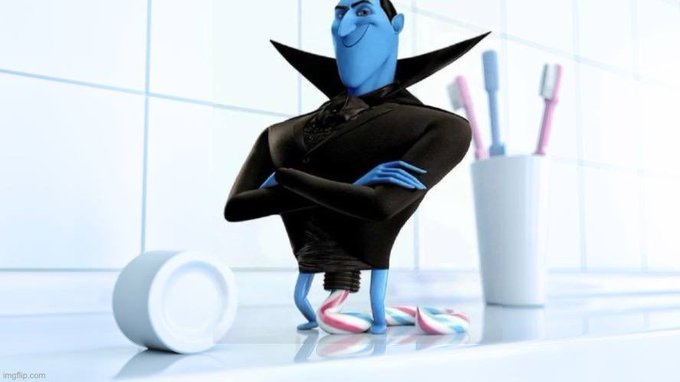 A 3D rendering of the character Megamind from the animated film, standing with arms crossed in a bathroom setting wearing his signature black suit with a large collar.