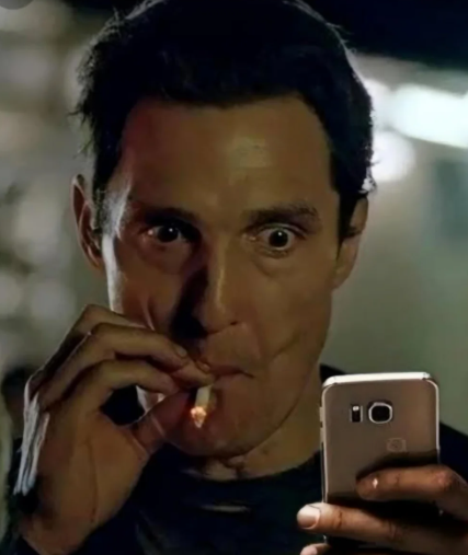 A close-up of a wide-eyed man smoking a cigarette while looking at a smartphone.