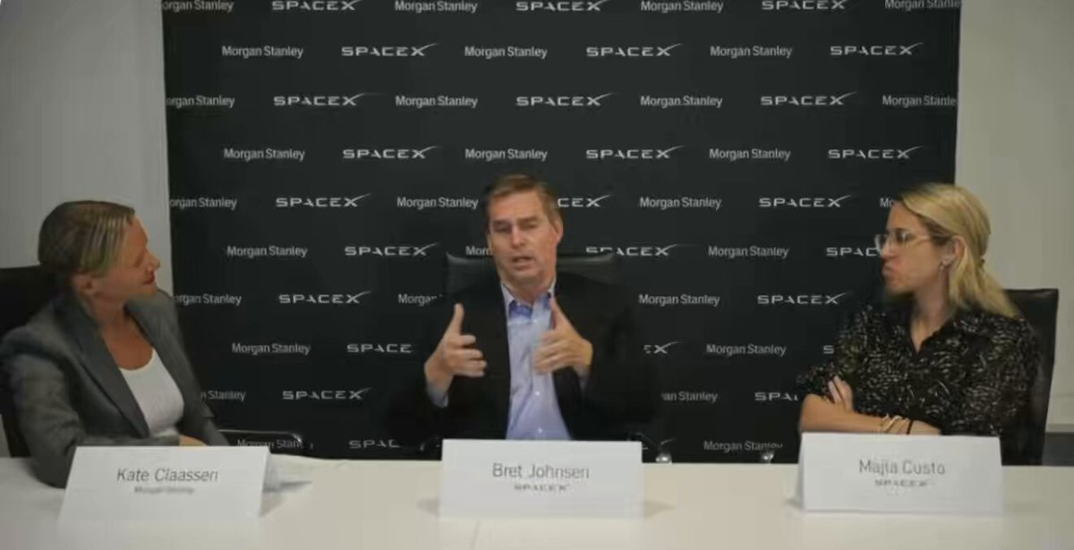 The image shows a group of three people sitting around a table, engaged in a discussion or interview. They are all wearing suits, indicating that they might be professionals involved in a business meeting or event. The background features a large black banner with white text, which reads "MOGUS STANLEY". This suggests that the gathering could be related to a company or organization named MOGUS STANLEY.