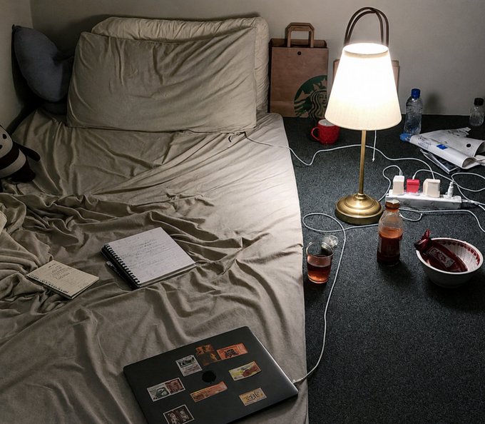 A cluttered hotel or bedroom floor beside an unmade bed displays a laptop covered in stickers, notebooks, a lit lamp, water bottles, a Starbucks paper bag, and a bowl of snacks—all connected by tangled cables. The scene humorously reinforces the caption's joke about crypto-savvy "bros" who amass significant $SOL holdings yet embrace a messy, bachelor-style living space.