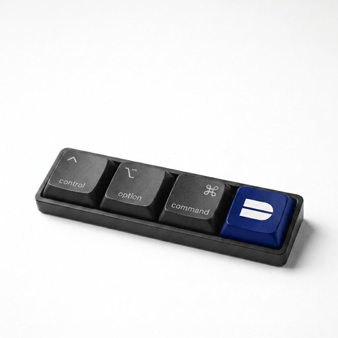 A black tray holding four novelty keycaps or macropads labeled 'control', 'option', 'command', and a blue split-bar icon, resembling Mac keyboard keys.