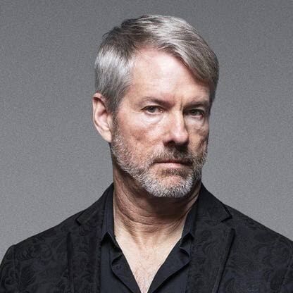 A portrait photo of a gray-haired man with a beard, wearing a black shirt and dark jacket, looking thoughtfully off to the side against a neutral gray background. The image appears unrelated to the accompanying post about Strategy's (formerly MicroStrategy) Bitcoin holdings and $STRC stock repurchase, suggesting the photo may have been shared incorrectly or is being used as a generic placeholder rather than depicting a figure directly connected to the announcement.