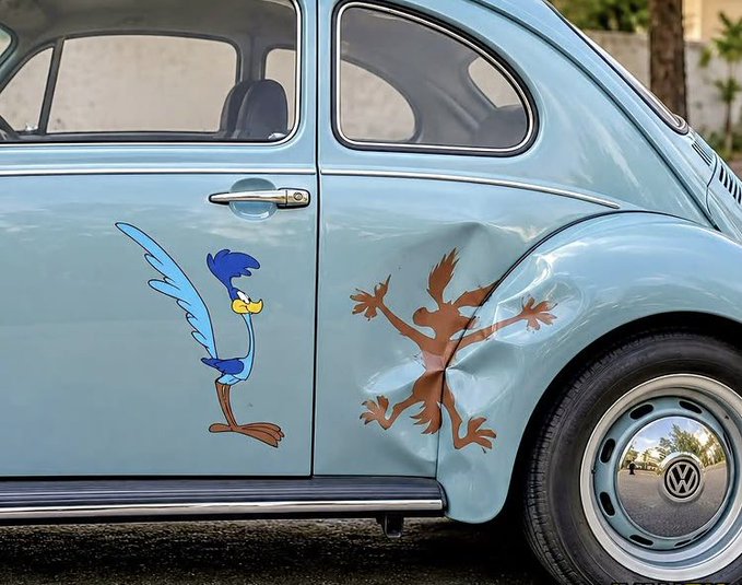 The side of a light blue Volkswagen Beetle with Road Runner decals on the door and a dent in the rear quarter panel where Wile E. Coyote appears to have crashed into it.