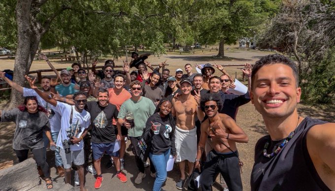 A smiling man takes a selfie with a large, energetic group of diverse participants posing together outdoors in a park, many throwing up peace signs and smiling broadly. The celebratory gathering reflects the post's message about a rewarding chapter at Lisk concluding after connecting with over 1,000 developers and founders across 10+ emerging market countries through tours, residencies, and hackathons.