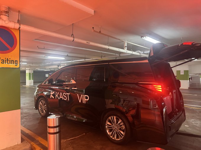 A black 'KAST VIP' minivan parked in a parking garage with its rear hatch open and brake lights illuminated.