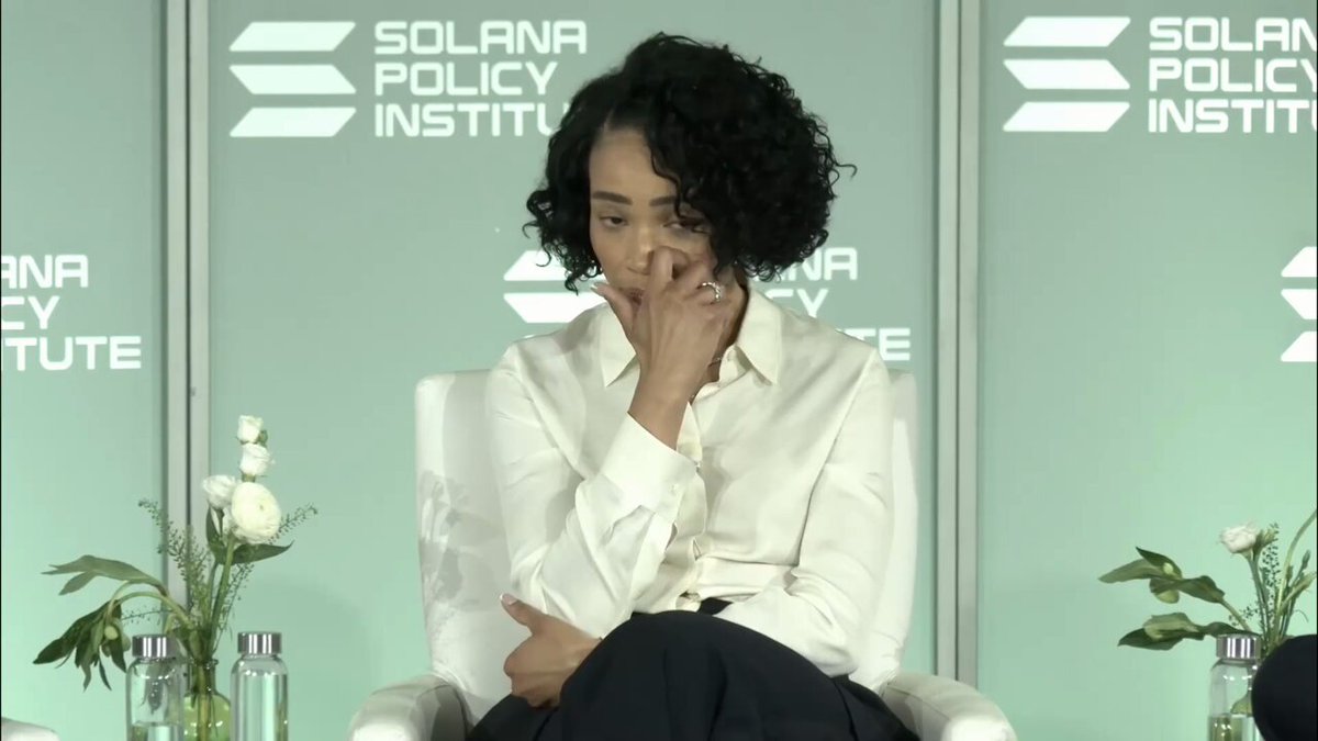 A woman in a white button-up shirt sits on stage at the Solana Policy Institute, her hand resting against her face in a contemplative pose, with the "Solana Policy Institute" logo visible on the green backdrop behind her. The image relates to the post as it captures a moment from what appears to be a policy discussion panel about federal crypto market structure legislation featuring speakers from WilmerHale and Gibson Dunn.