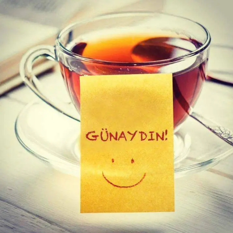 A glass cup of tea with a yellow paper tag reading 'GÜNAYDIN!' (Turkish for 'Good morning!') featuring a smiley face.