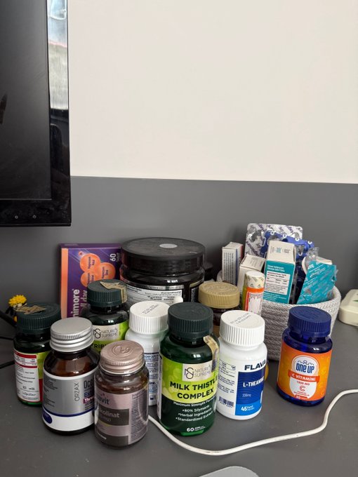 A collection of supplement bottles on a counter, including Milk Thistle Complete, Flaxseed L-Theanine, and an orange AAA Up bottle, along with other health products.