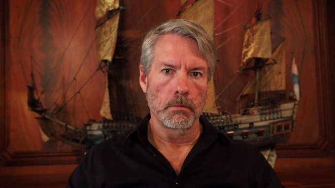 Michael Saylor poses in front of a large model ship painting, his stern expression reflecting the post's portrayal of him as intensely devoted to $MSTR, likening his single-minded commitment to the company to a captain wholly devoted to his vessel.