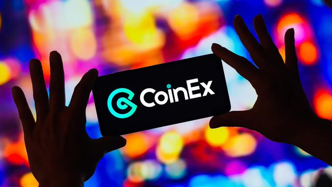 Silhouetted hands holding a smartphone displaying the CoinEx logo against a colorful, blurred neon-lit background.