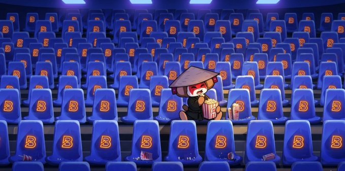 A small cartoon character wearing a conical hat and sitting alone in a large cinema, eating popcorn, surrounded by rows of empty blue seats marked with the letter 'B'.