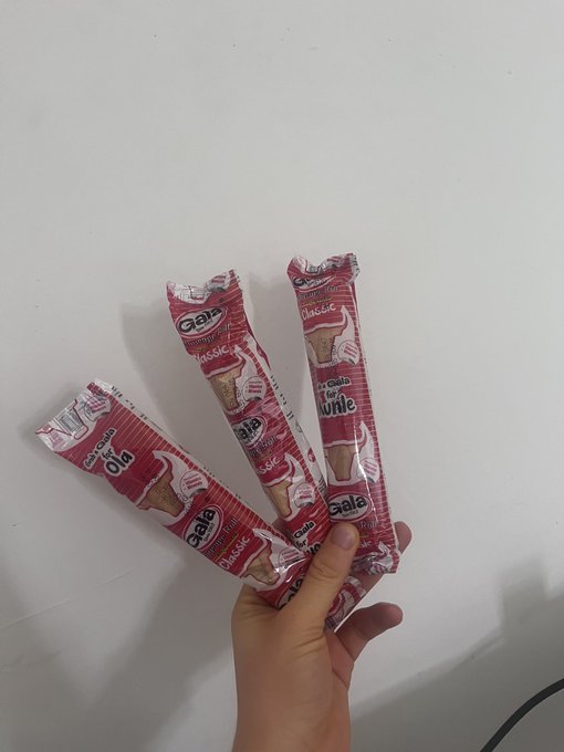A hand holding four red-wrapped Gala ice cream biscuit sticks against a plain white background.