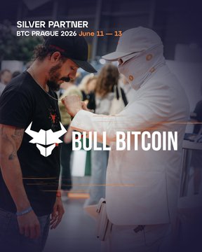 The image features a man wearing a black shirt, standing next to another person who is wearing a white hat. They are both looking at each other while surrounded by several people. The background of the image includes text that reads "Silver partner", "BTC Prague", and "June 11 - 13". Additionally, there's an advertisement for "Bull BitCoin" in the form of a poster or banner with the words "Legendary @BULLBITCOIN is in Prague. Will you be there too?".