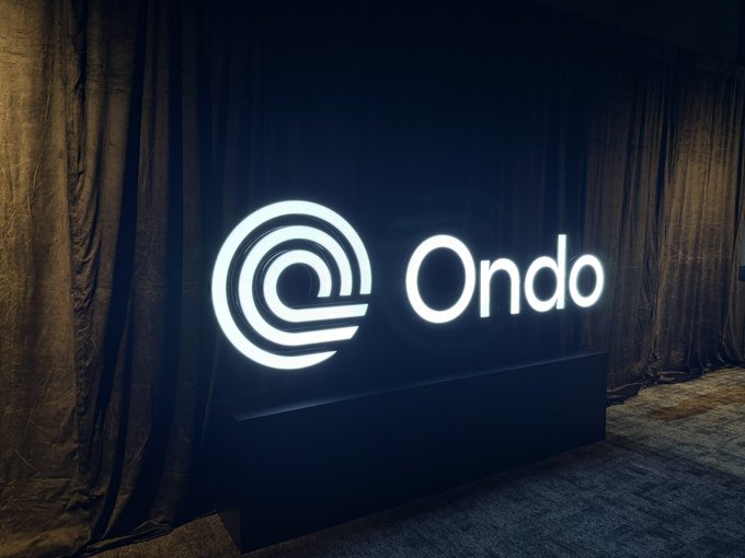 An illuminated "Ondo" sign glows against a dark curtain backdrop, marking the venue for Ondo's "Open Interest" event in Singapore, where attendees from major financial institutions like Franklin Templeton gathered to discuss key industry topics.