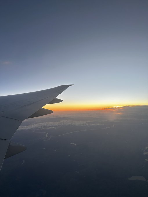 An airplane wing silhouettes against a sunrise over clouds, capturing the journey of moving to the USA to pursue $450K in PhD funding for AI/ML research in mechanical engineering. The image evokes the excitement and fresh start of this next chapter.