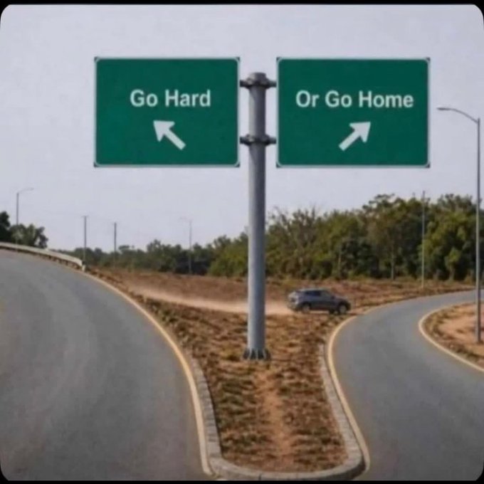 A road sign at a fork in the road shows two options: "Go Hard" pointing left and "Or Go Home" pointing right.