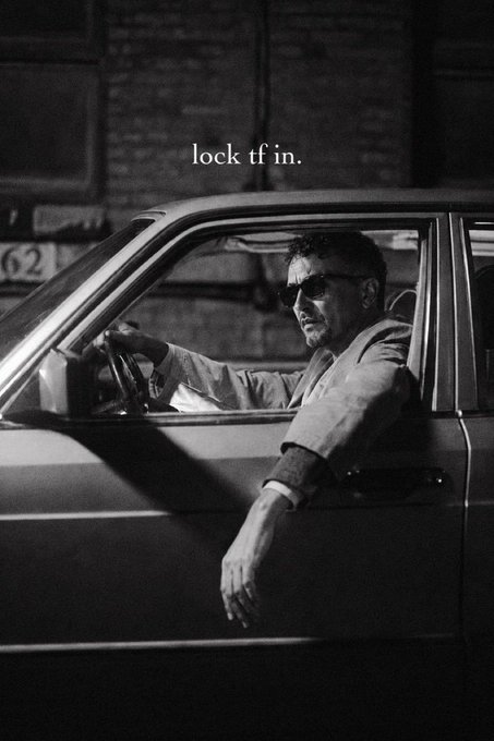 Black and white photo of a man in sunglasses and a suit sitting in a car with the text 'lock tf in.' overlaid.