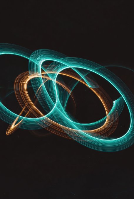 An abstract light painting featuring swirling, intertwined ribbons of teal and orange light against a black background.