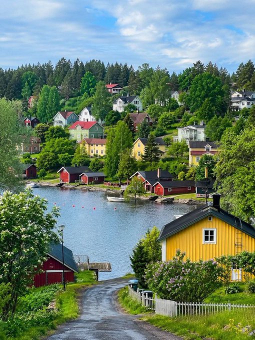 A scenic view of a colorful coastal village with red, yellow, and white houses built along a hillside beside a calm blue waterway.