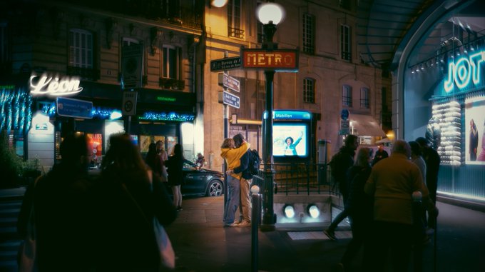 A nighttime street scene in Paris featuring a couple embracing under a glowing 'METRO' sign, with neon-lit storefronts including 'Léon' and 'JOY' in the background and pedestrians walking by.
