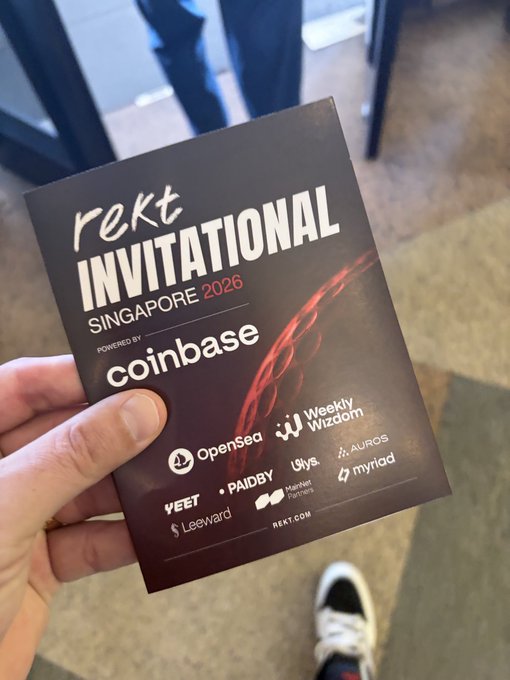 A hand holding a 'rekt INVITATIONAL SINGAPORE 2026' event pass powered by Coinbase, with sponsors including OpenSea, Weeklyzdom, Aurous, YEET, PAIDBY, Ulys, mynad, Leeward, and Manifest Partners.