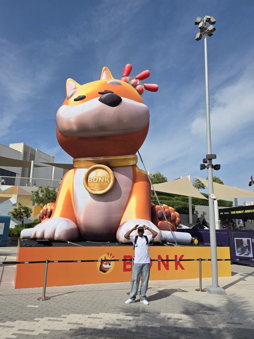 A man poses with arms raised in a playful stance in front of a giant inflatable dog mascot with "BONK" written on its medallion and base, matching the post's enthusiastic "Lets Bonk it today" sentiment.